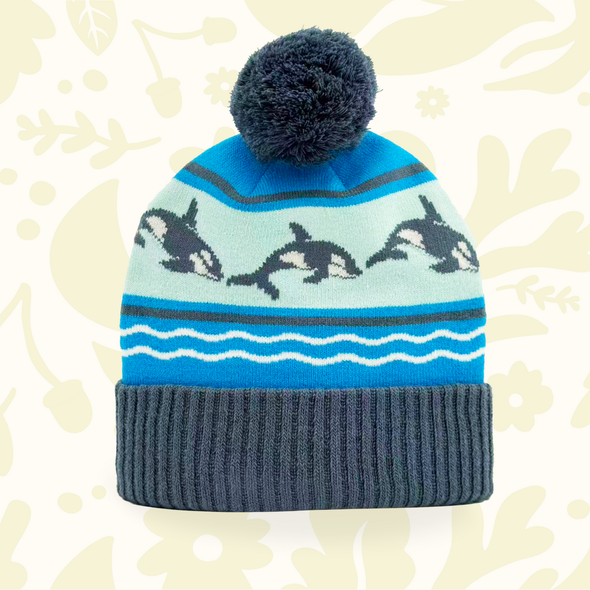 Forager Provisions LTD knit beanie in blue with a jumping orca whale pattern, wave motifs, and a dark grey pom-pom.