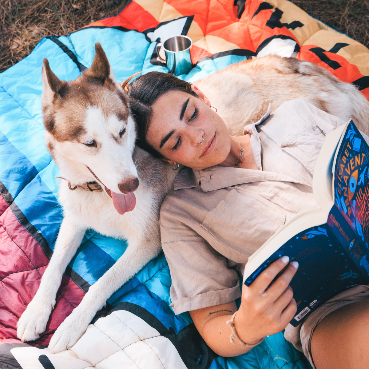 Forager Provisions LTD Seven Peaks van life comforter with a woman reading a book next to her husky dog outdoors