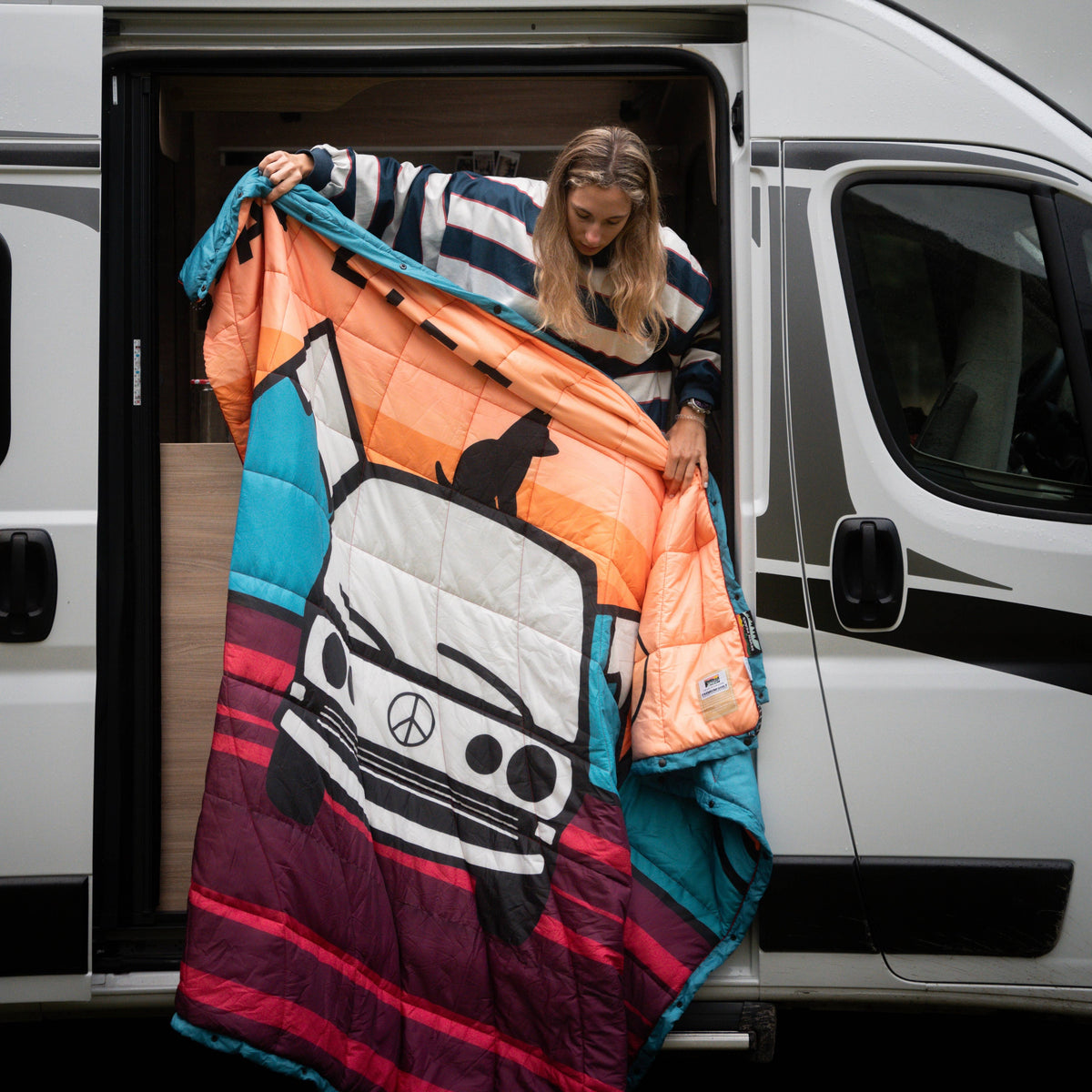 Forager Provisions LTD Seven Peaks van life comforter with colourful campervan graphic held by a woman at a van door