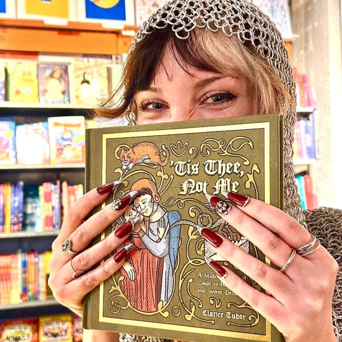 Forager Provisions LTD signed copy of Tis Thee, Not Me by Clarice Tudor, held by a woman wearing a chainmail coif.