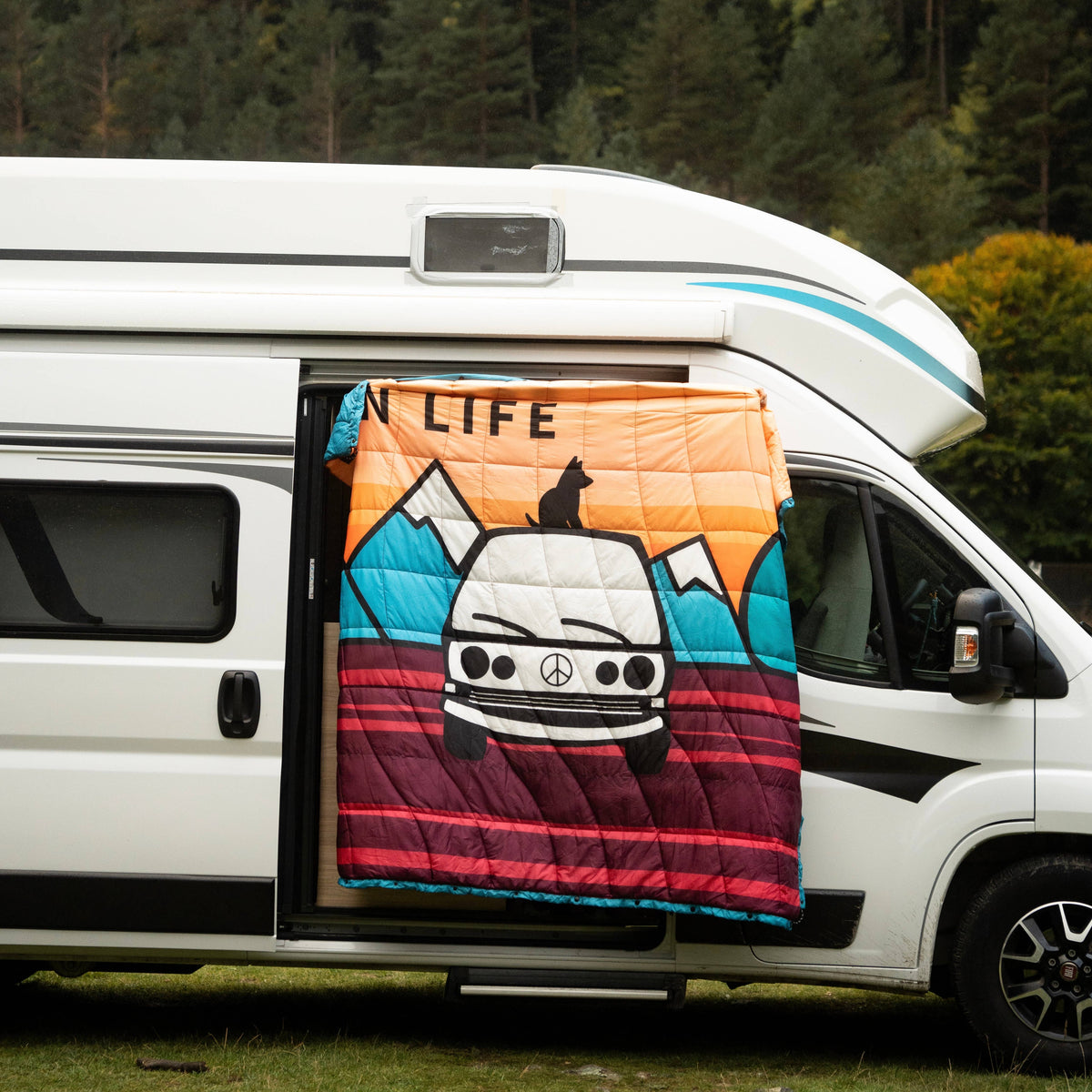 Forager Provisions LTD Seven Peaks van life comforter with adventure graphic hanging on a campervan door in a forest.