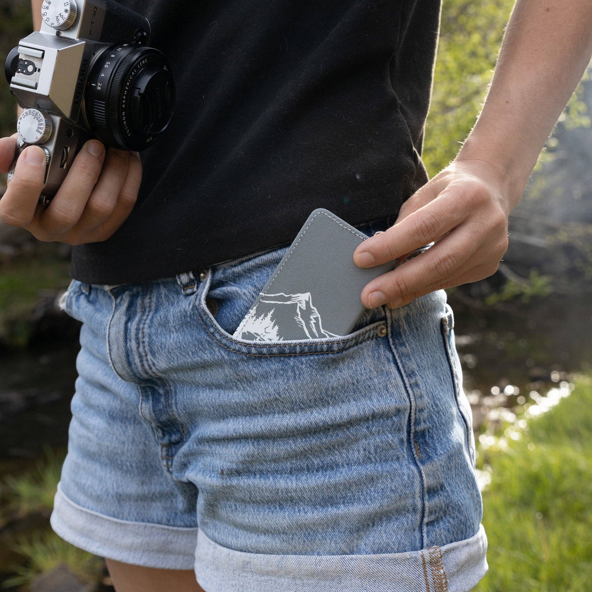 Forager Provisions LTD Wildtree Wilderness card holder with mountain design being placed into denim shorts pocket