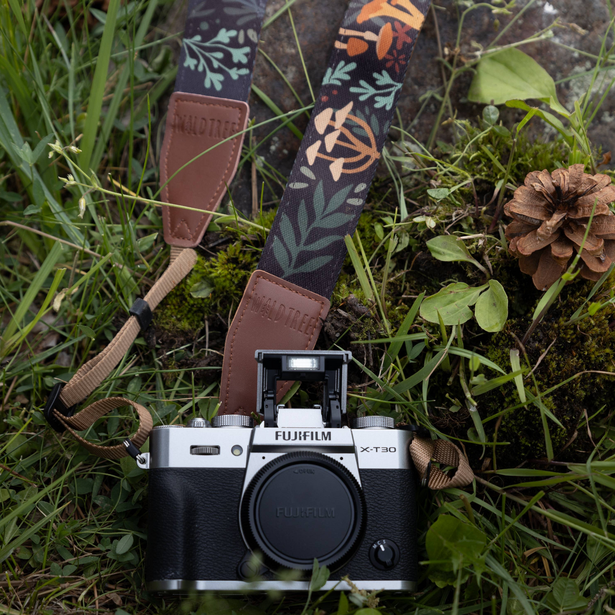 Forager Provisions LTD Wildtree camera strap with mushroom and foliage print attached to a Fujifilm camera in grass.