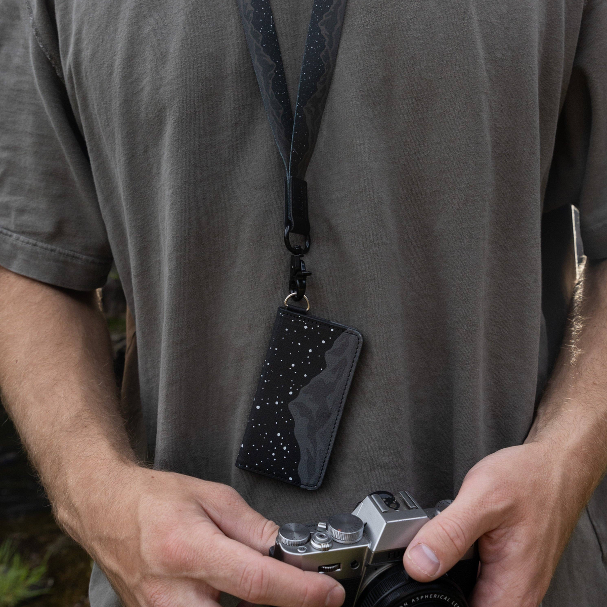 Forager Provisions LTD Wildtree Midnight Mountain card holder hanging from a lanyard, held by a person with a camera.