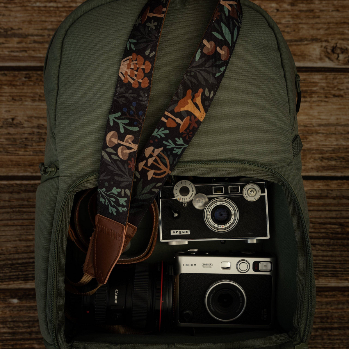 Forager Provisions LTD Wildtree Forest Foliage camera strap with mushroom print inside a green backpack with two cameras.