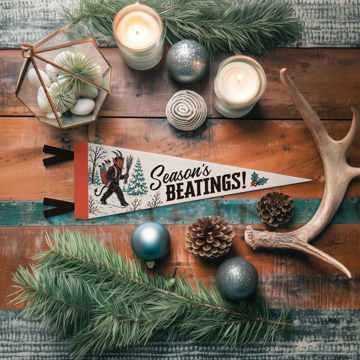 Forager Provisions LTD Season's Beatings Krampus felt pennant on a rustic wooden table with pine, candles, and ornaments.
