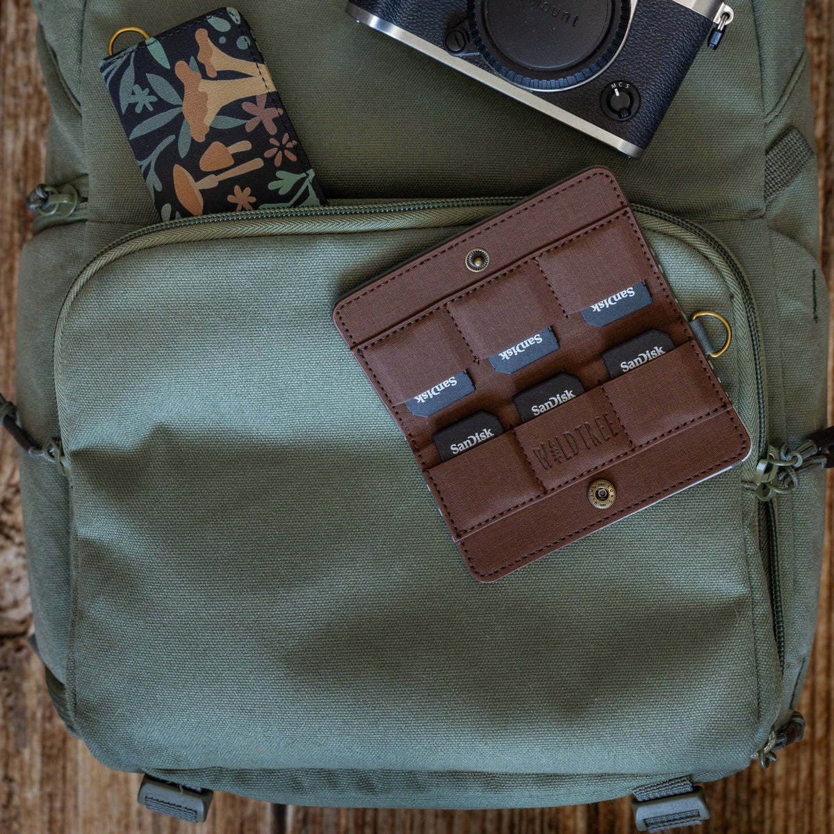 Forager Provisions LTD Wildtree Forest Foliage card holder with SD cards, camera, and backpack on a wooden surface.