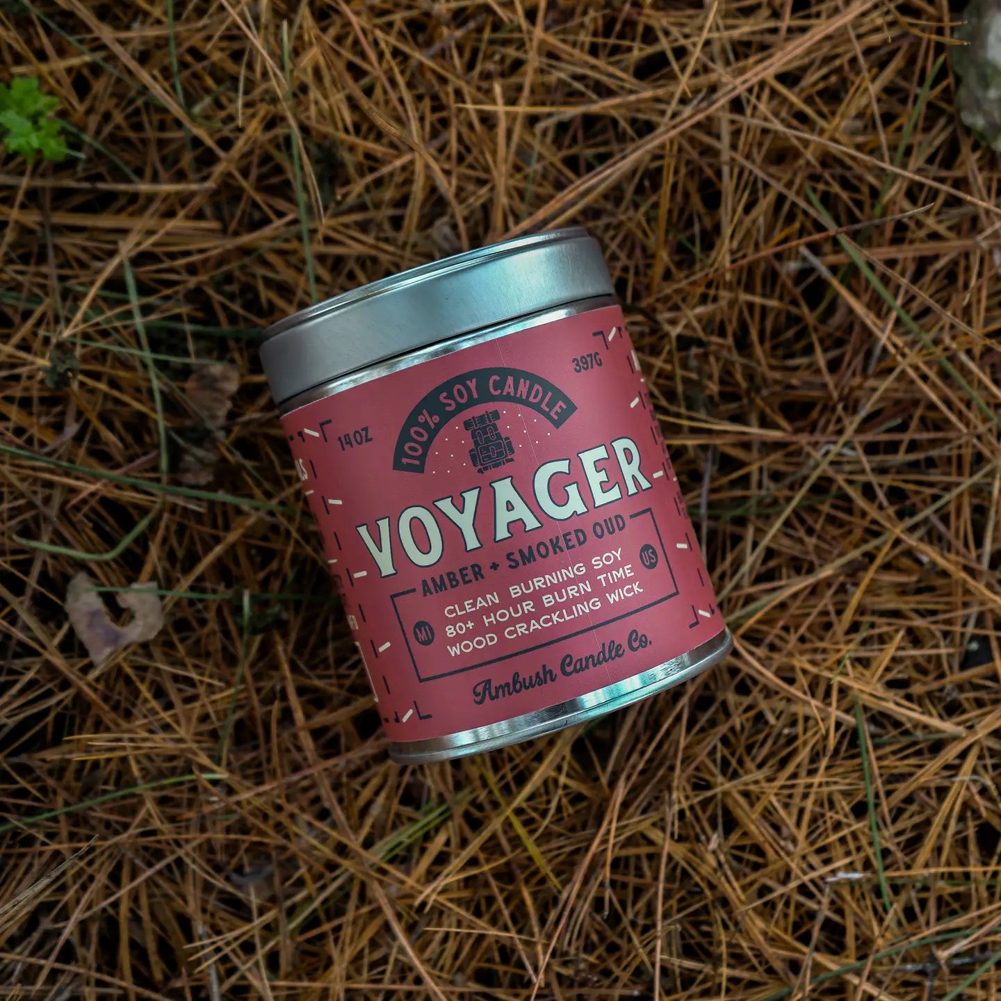 14oz Ambush Candle Co Voyager Amber & Smoked Oud soy candle featured outdoors on pine needles; luxury scented candle display.