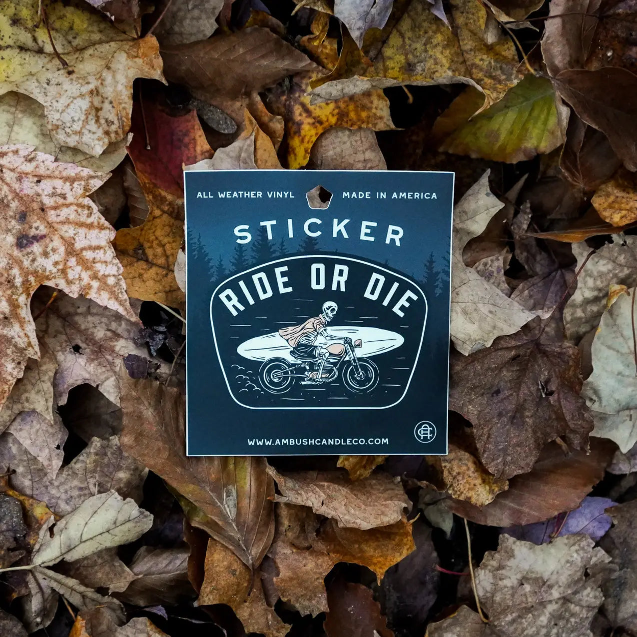 The Ambush Candle Co Ride or Die Sticker showcases a motorcyclist riding through fallen autumn leaves. The text on the sticker reads, "All Weather Vinyl, Made in America," highlighting its rugged durability that is both dishwasher safe and weatherproof.