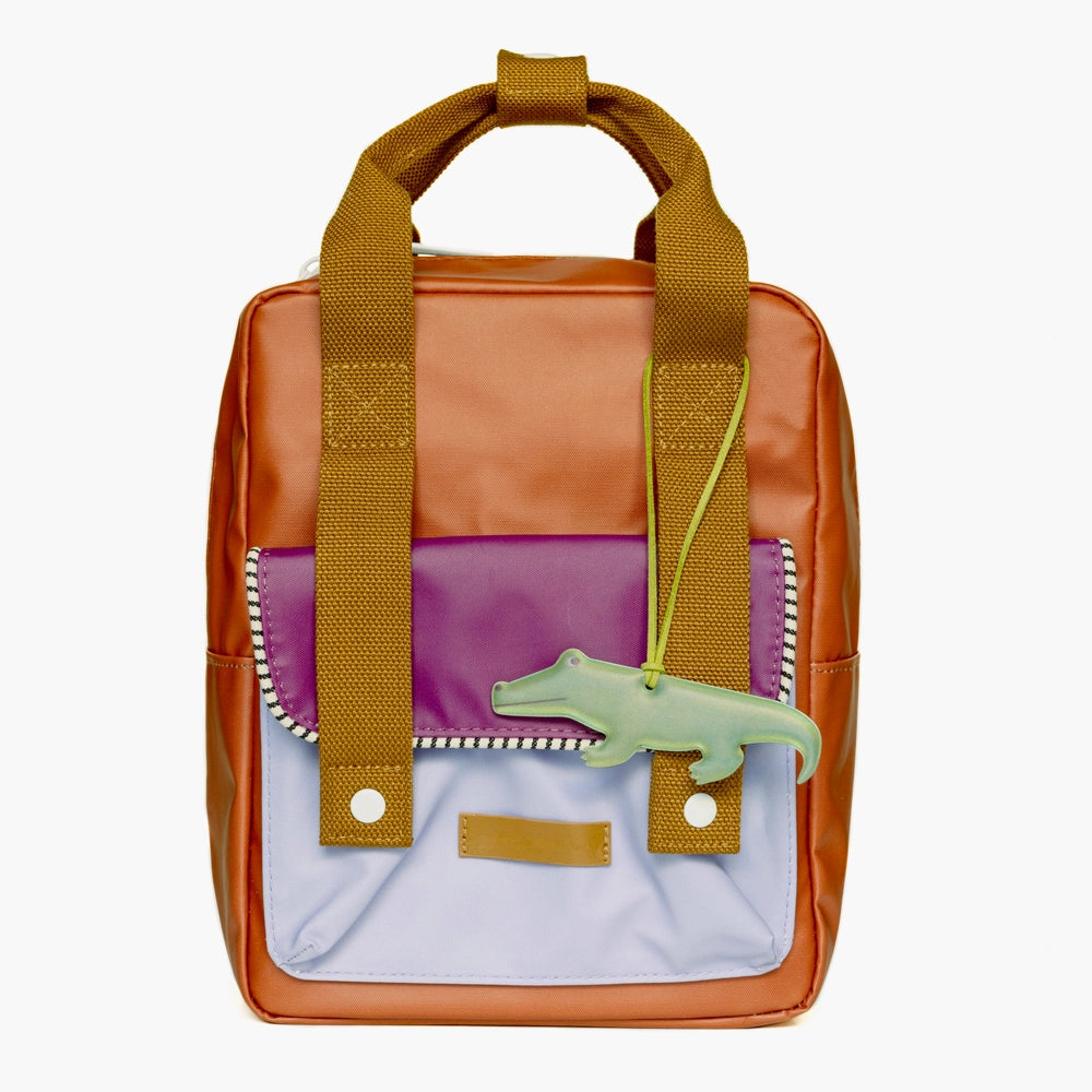 Trendy multicolored backpack with wide brown straps, featuring a Firefly Sweden Crocodile Reflector charm on the zipper.
