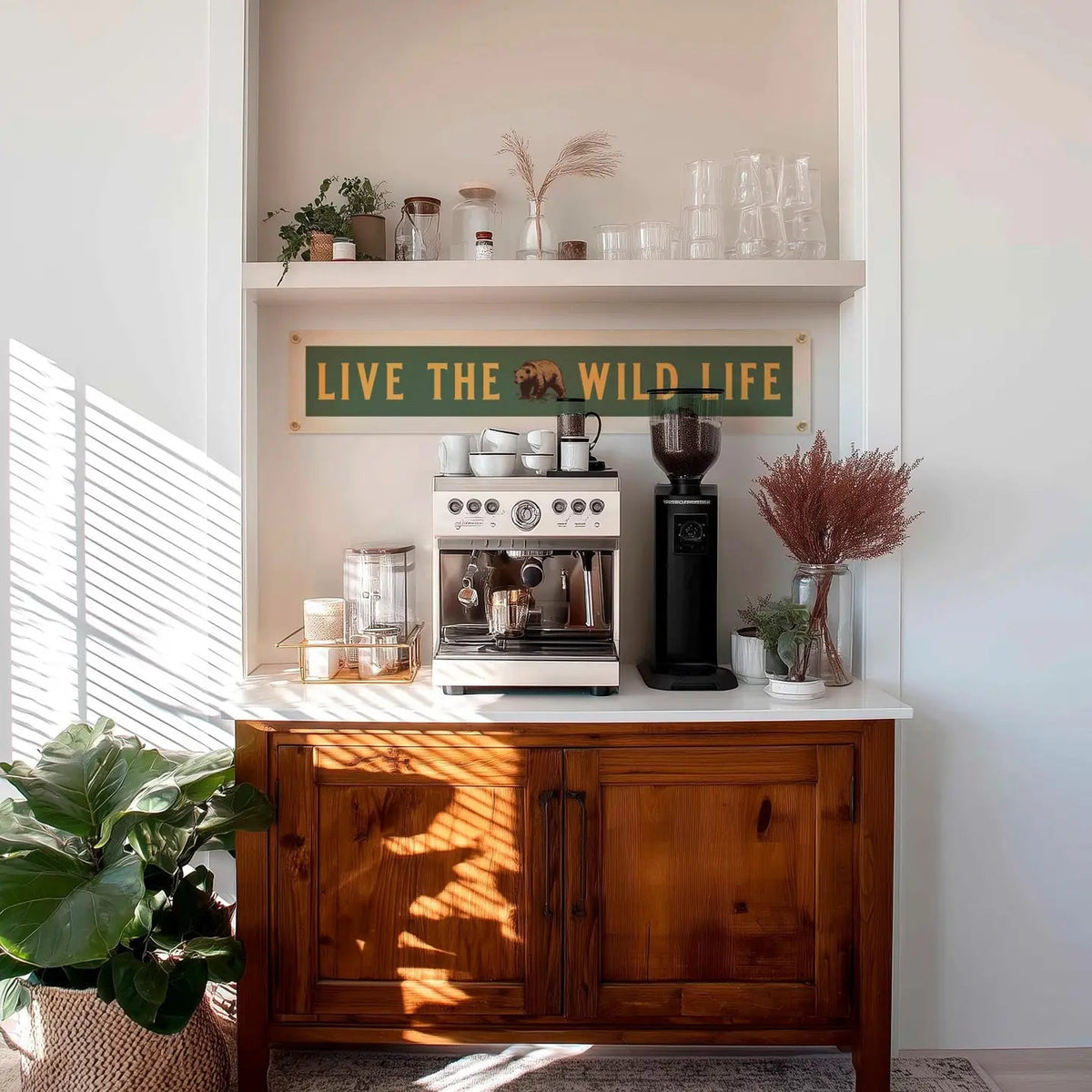 Coffee station with espresso machine, mugs, plants, vintage camping decor, and Benoit’s Live The Wild Life felt banner sign.