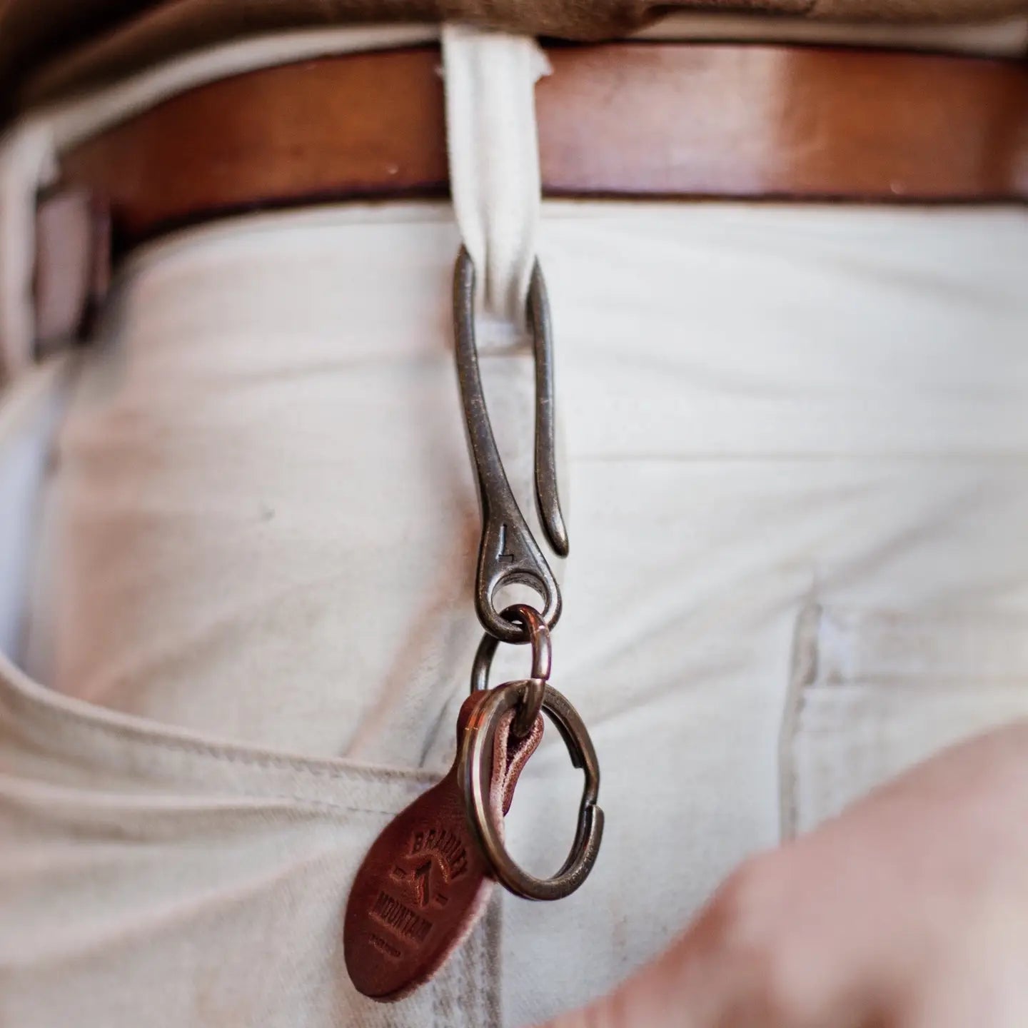 Bradley Mountain Brass Fish Hook Key Fob attached to a white pants belt loop, brown leather belt, stylish everyday carry accessory.
