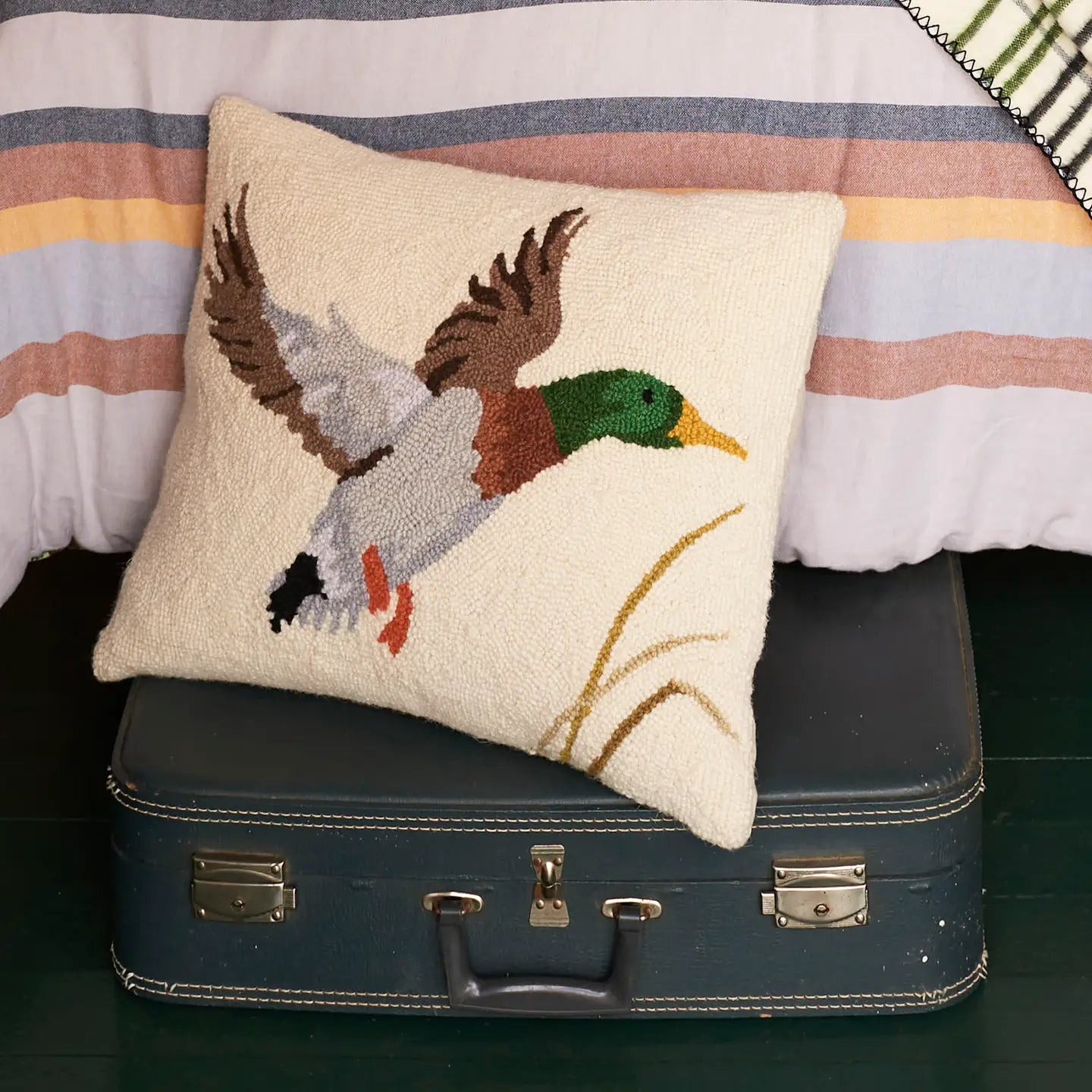 Camp Wandawega Mallard Hook Pillow by Peking on vintage suitcase in front of striped bedspread, rustic cabin decor style.