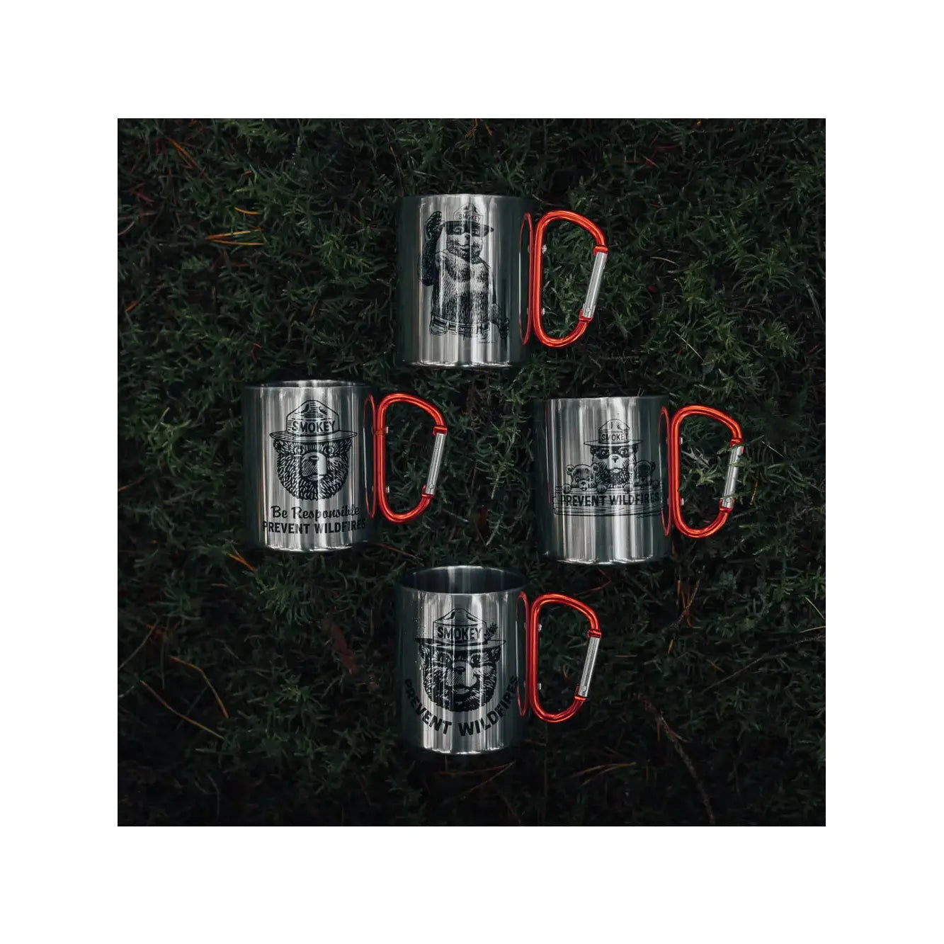 The Smokey Bear Carabiner Handle Mug - Waving Smokey is a silver mug that showcases an illustration of Smokey Bear wearing a ranger hat, featuring a vibrant red carabiner handle to promote wildfire prevention.