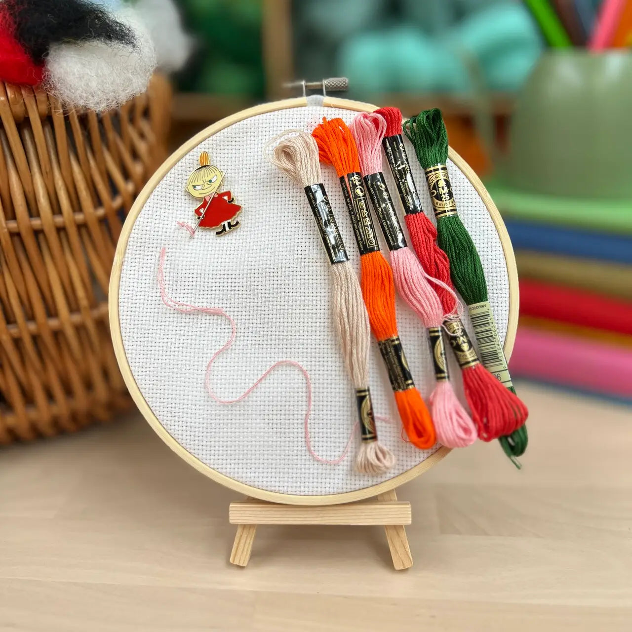 The Crafty Kit Co Moomin Needle Minder features a Little My character with a mischievous expression, dressed in red and holding a needle with pink thread. This charming embroidery accessory comes equipped with a strong magnet to keep your project secure.