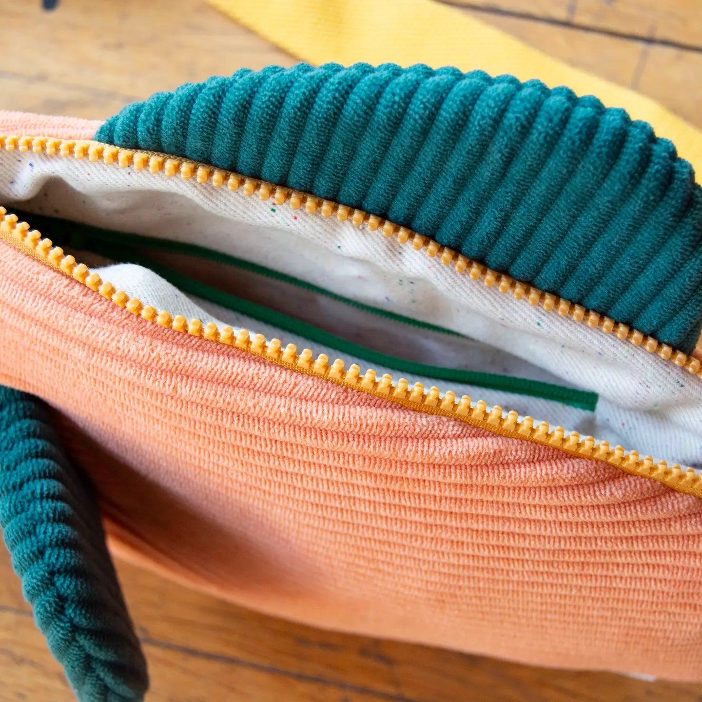 Curlworks Fish Bag crossbody in coral salmon & dark green with yellow zipper, stylishly displayed on wood, fashion accessory.