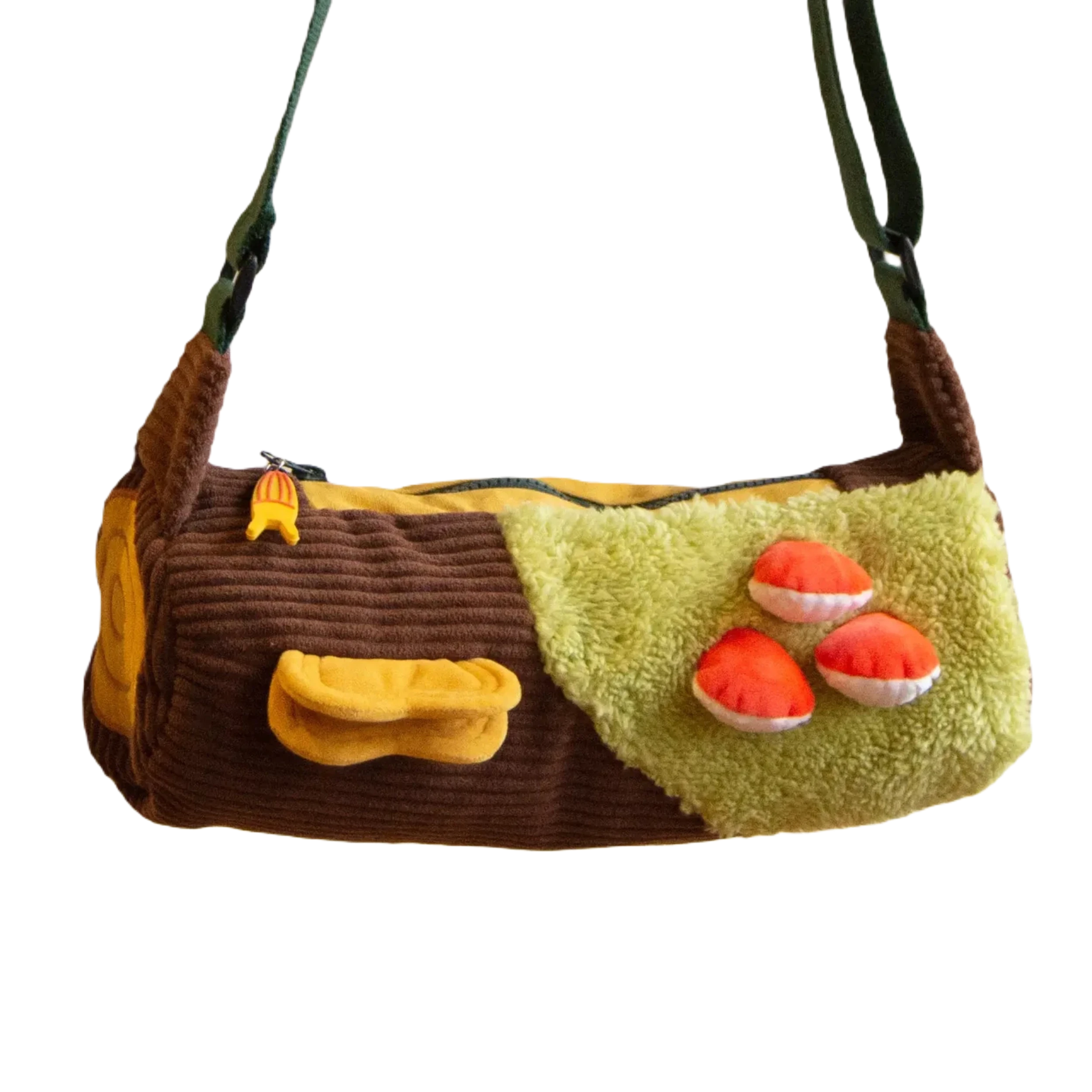 Introducing the Curlworks Toadstool Log Bag: a whimsical plush accessory designed to resemble a log, complete with lush green moss and tiny orange mushrooms. It boasts a distinctive banana slug zipper pull and an enchanting green strap for added appeal.
