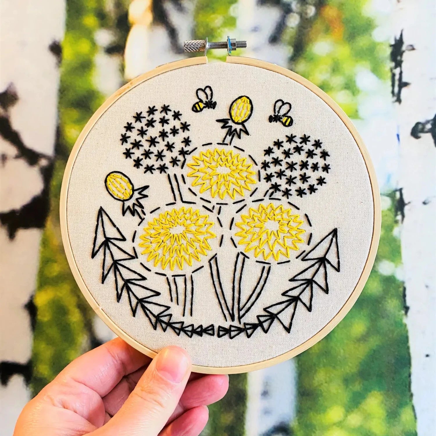 The Hook Line & Tinker Complete Embroidery Kit - Dandelion showcases beige fabric adorned with yellow flowers, black stems, leaves, and two bees. This beginner-friendly embroidery kit is entirely plastic-free.