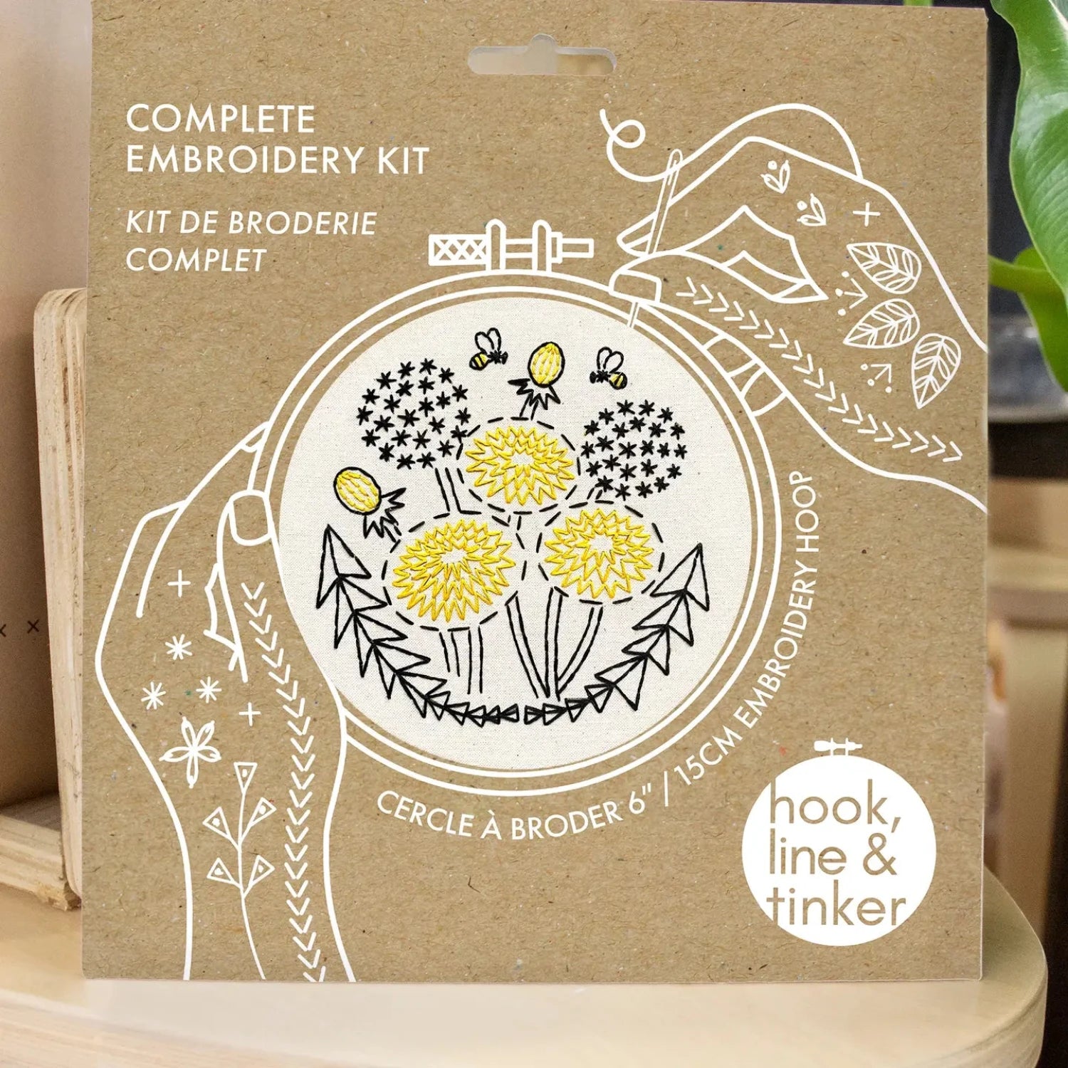 The Hook Line & Tinker Complete Embroidery Kit - Dandelion showcases beige fabric adorned with yellow flowers, black stems, leaves, and two bees. This beginner-friendly embroidery kit is entirely plastic-free.