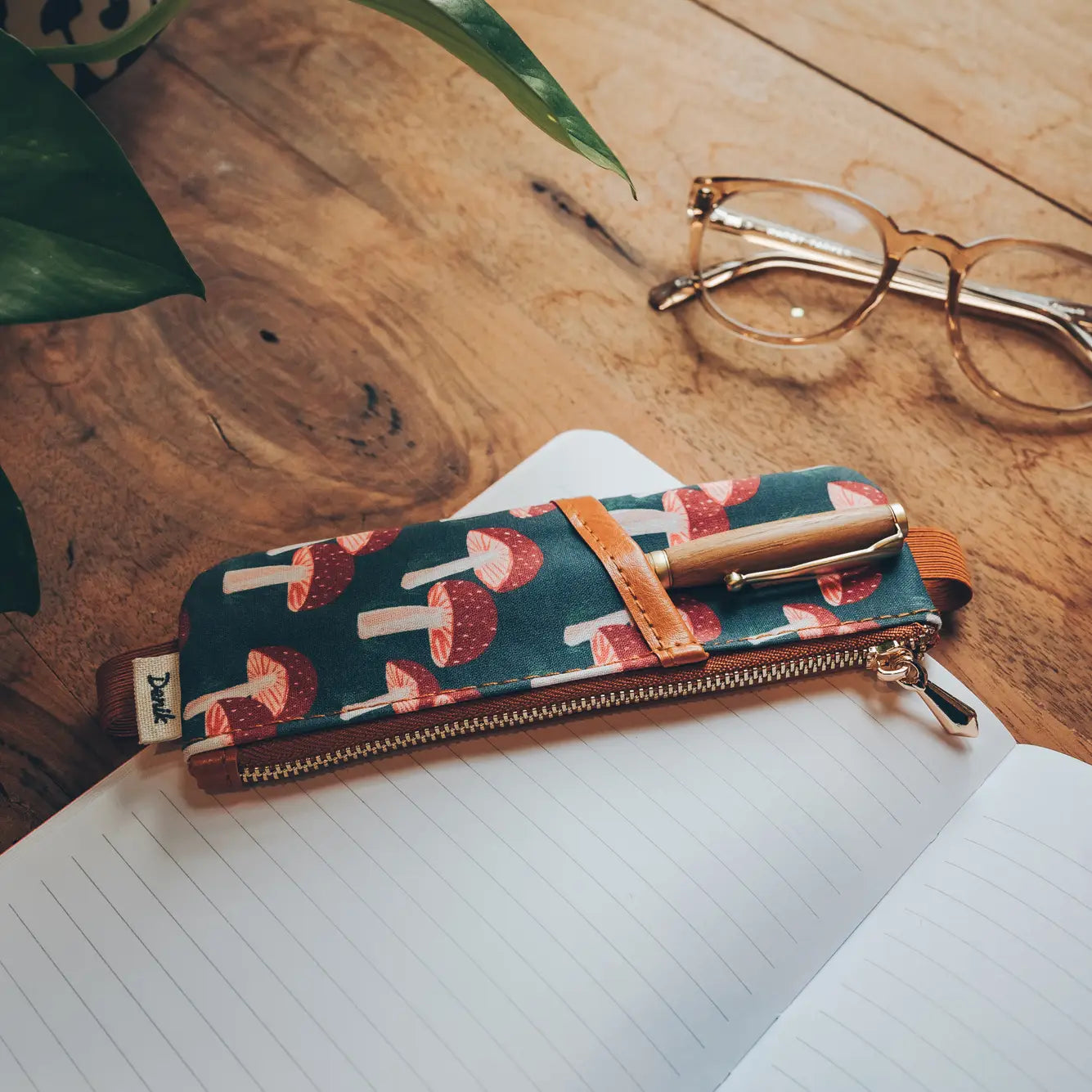Denik Navy Mushroom Vegan Leather Notebook Pouch on wooden desk with open notebook and eyeglasses—stylish stationery accessory.