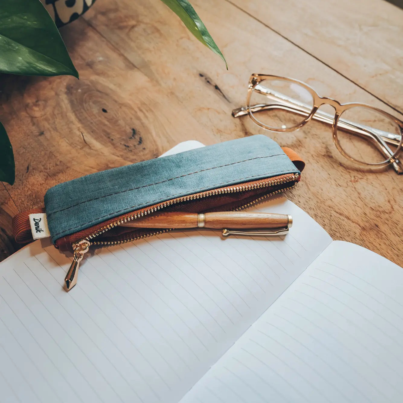 Denik Denim Distressed Blue Notebook Pouch on wood table, with notebook, gold pen, eyeglasses—perfect back to school accessory.