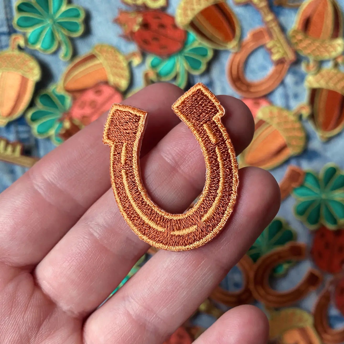 Hand holding small orange horseshoe patch from Kate O’Hara Good Luck Embroidered Patch Set, unique iron-on accessory.