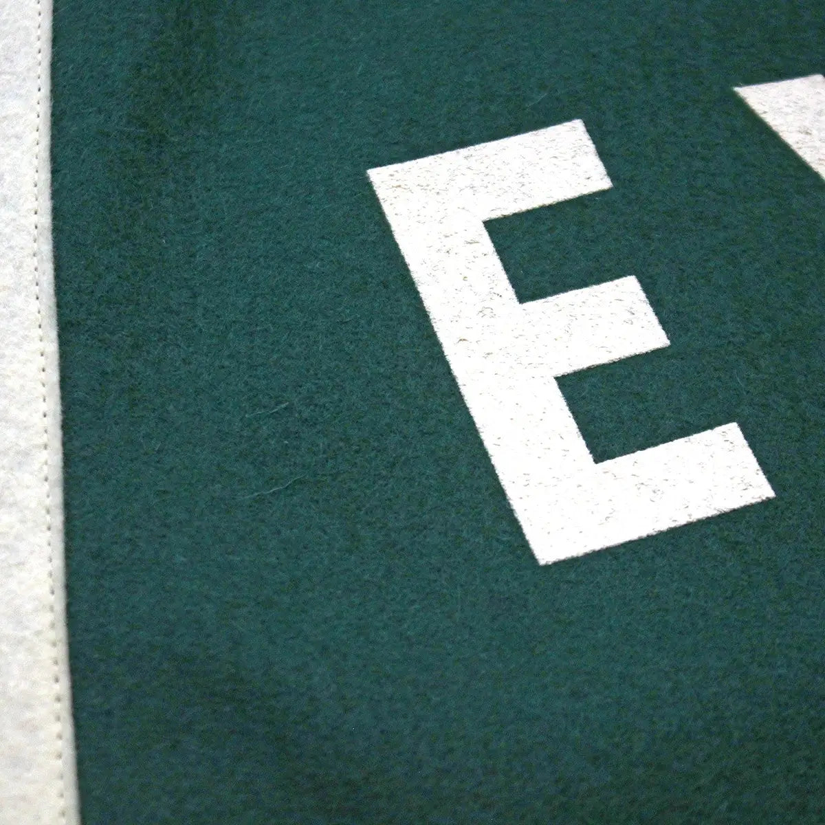 Close-up of Oxford Pennant EXPLORE camp flag, green wool felt, white trim, partial letter E—vintage banner outdoor decor.