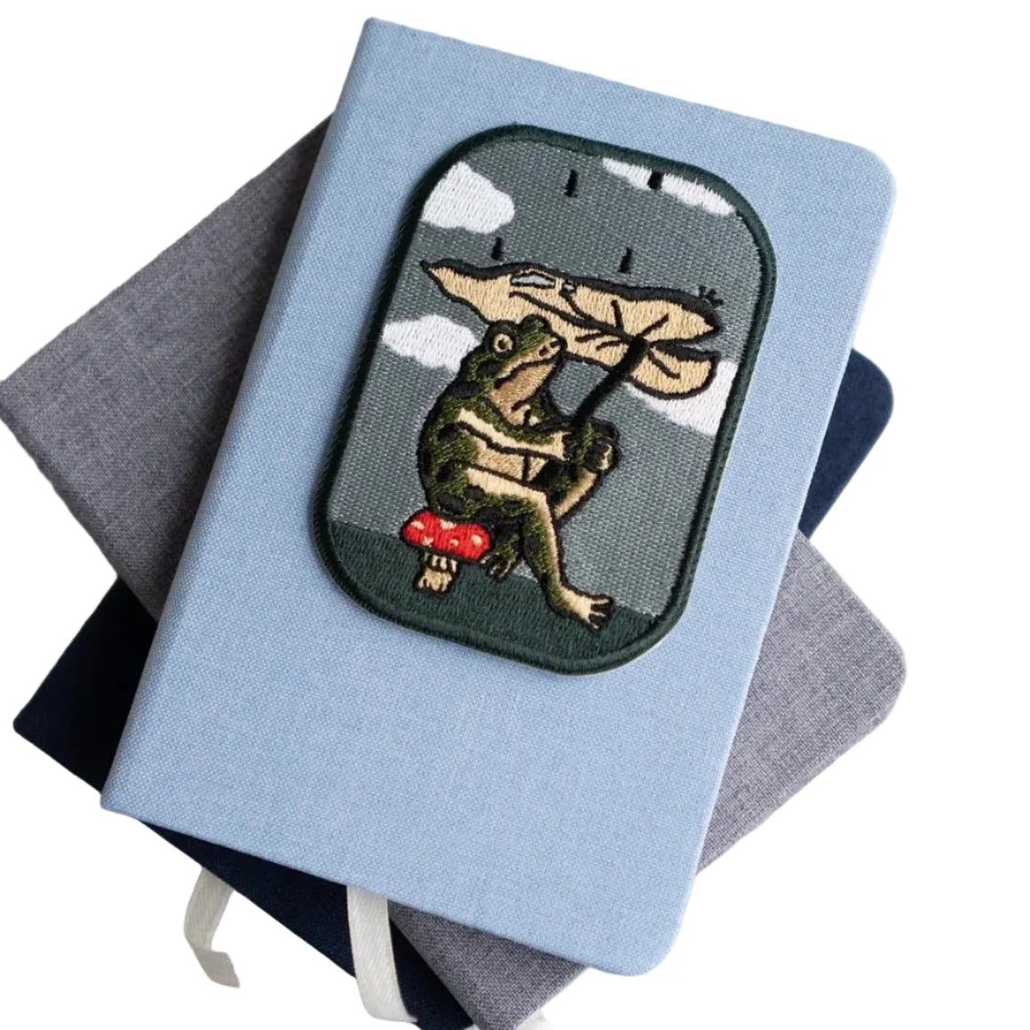 Stay Home Club blue notebook with frog leaf patch sits atop two plain notebooks—perfect cute stationery for students and journaling.