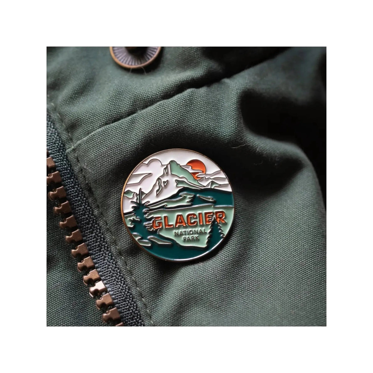 The Landmark Project Glacier National Park Pin is a round enamel pin featuring a mountain and river design with the text "GLACIER NATIONAL PARK." Attached to a green fabric backing, this pin celebrates Glacier National Park and highlights our dedication to sustainable packaging, making it an ideal addition for enamel pin collectors.