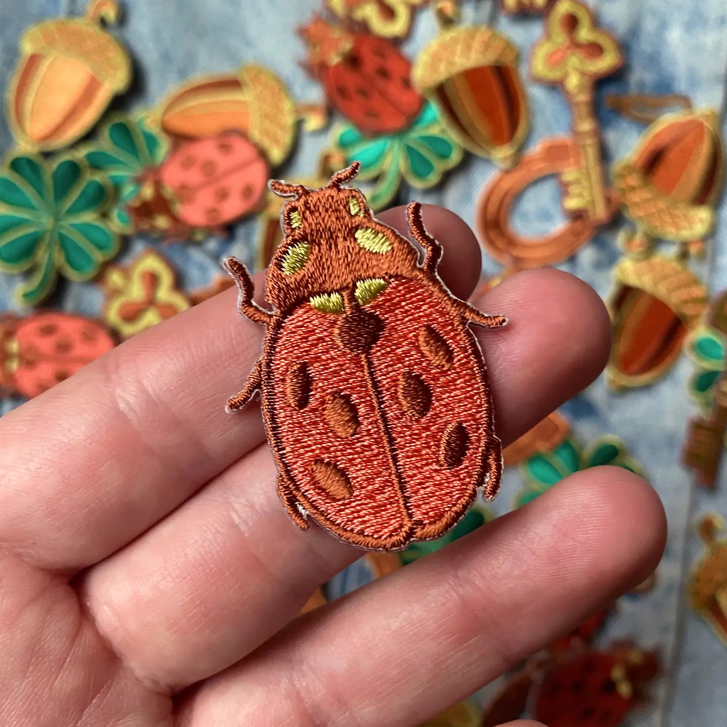 Hand holds Kate O’Hara Good Luck Embroidered Patch, vibrant embroidery, others from 5 Patch Set scattered in background.