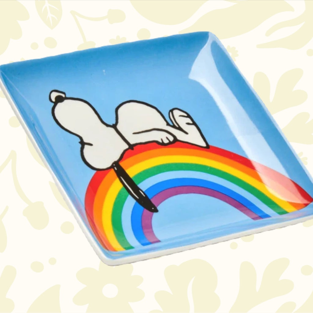 A blue box features a drawing of Snoopy lying on a rainbow, with text that reads "Magpie + Peanuts comic strip" at the top and "Good Vibes Trinket Tray" at the bottom.