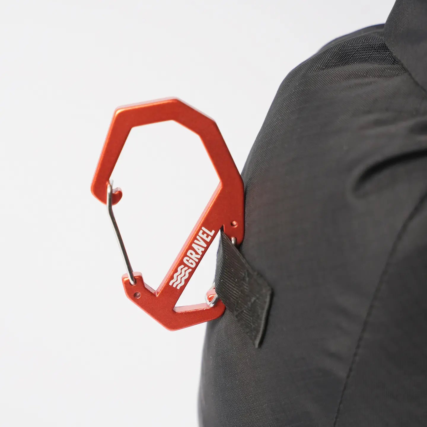 Orange carabiner attached to a gray backpack on a white background