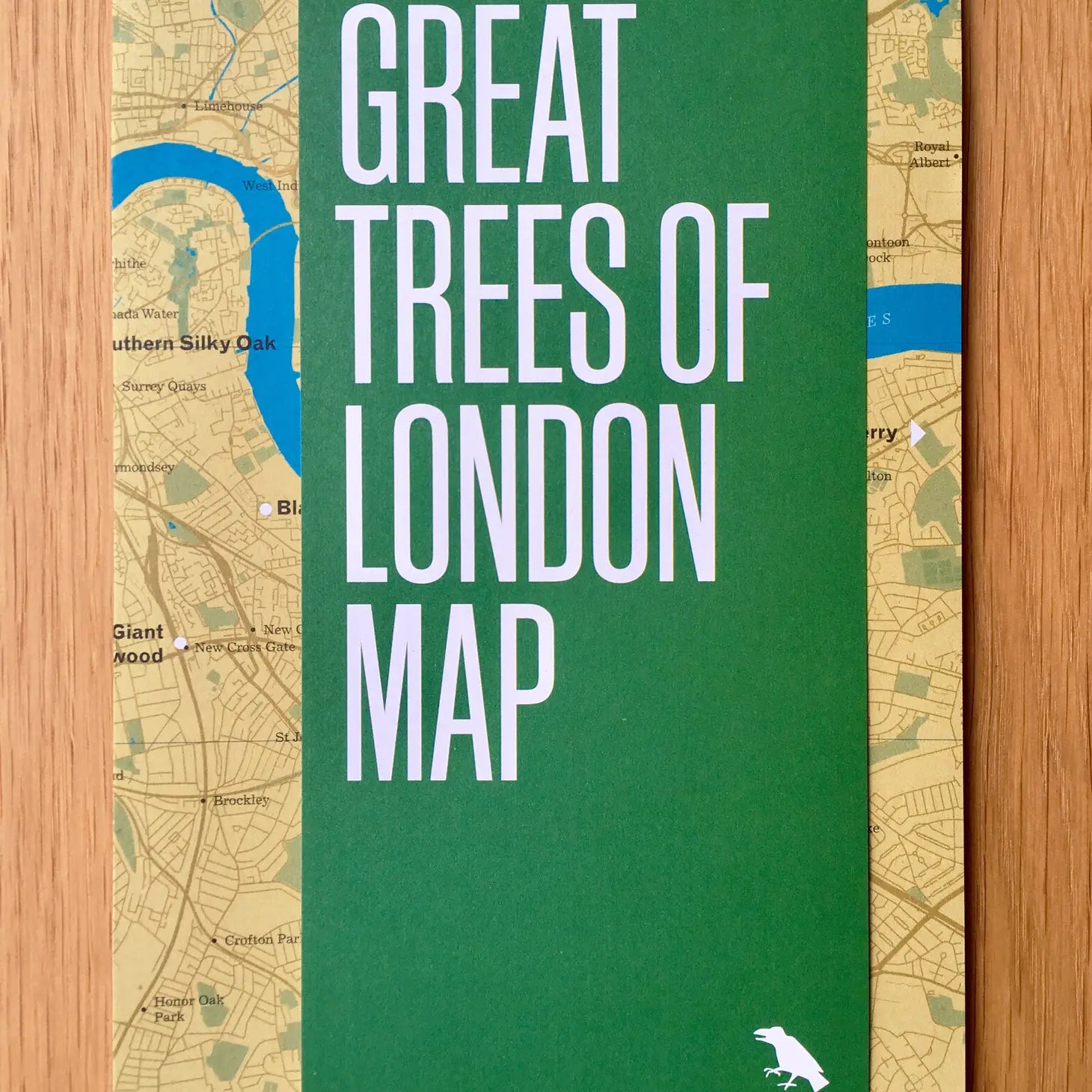 Cover of the "Blue Crow Media Great Trees Of London Map" featuring a green title block overlaid on a detailed map of London's areas, printed on recycled FSC-certified paper, all displayed on a wooden surface.