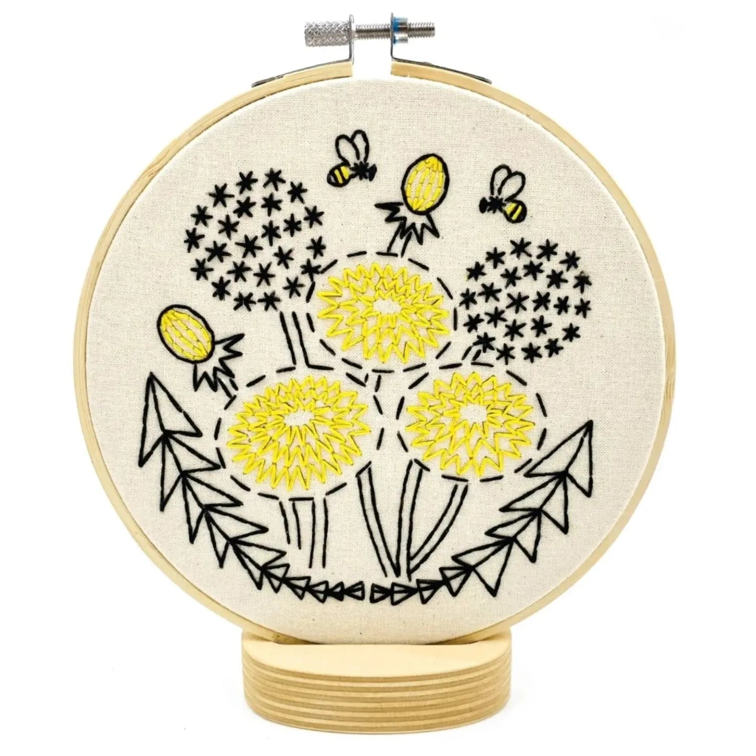The Hook Line & Tinker Complete Embroidery Kit - Dandelion showcases beige fabric adorned with yellow flowers, black stems, leaves, and two bees. This beginner-friendly embroidery kit is entirely plastic-free.