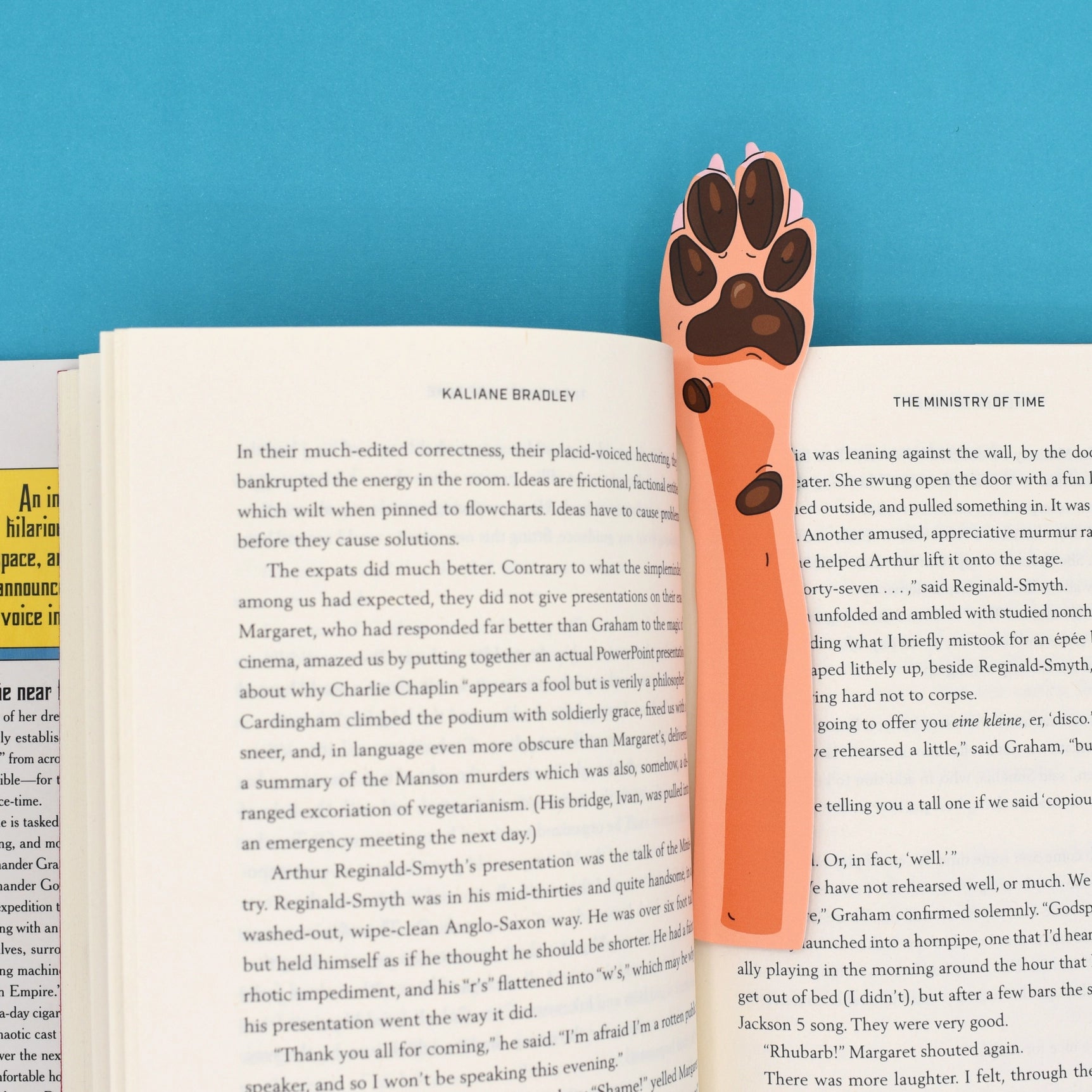 Die cut dog paw bookmark on open book, blue background; cute stationery gift for readers, pet lovers, book accessories.