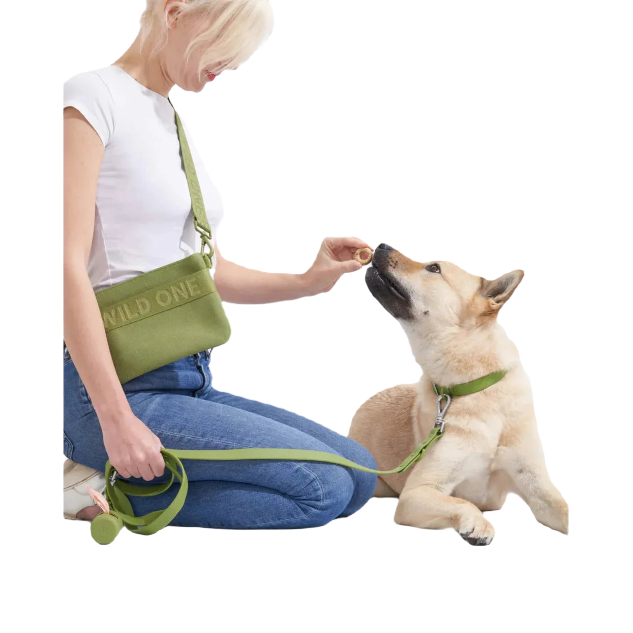 The Wild One Dog Poop Bag Dispenser Holder in Moss is a green cylindrical container with a strap, dispensing pink poop bags from a side opening and featuring an eco-friendly leash attachment.