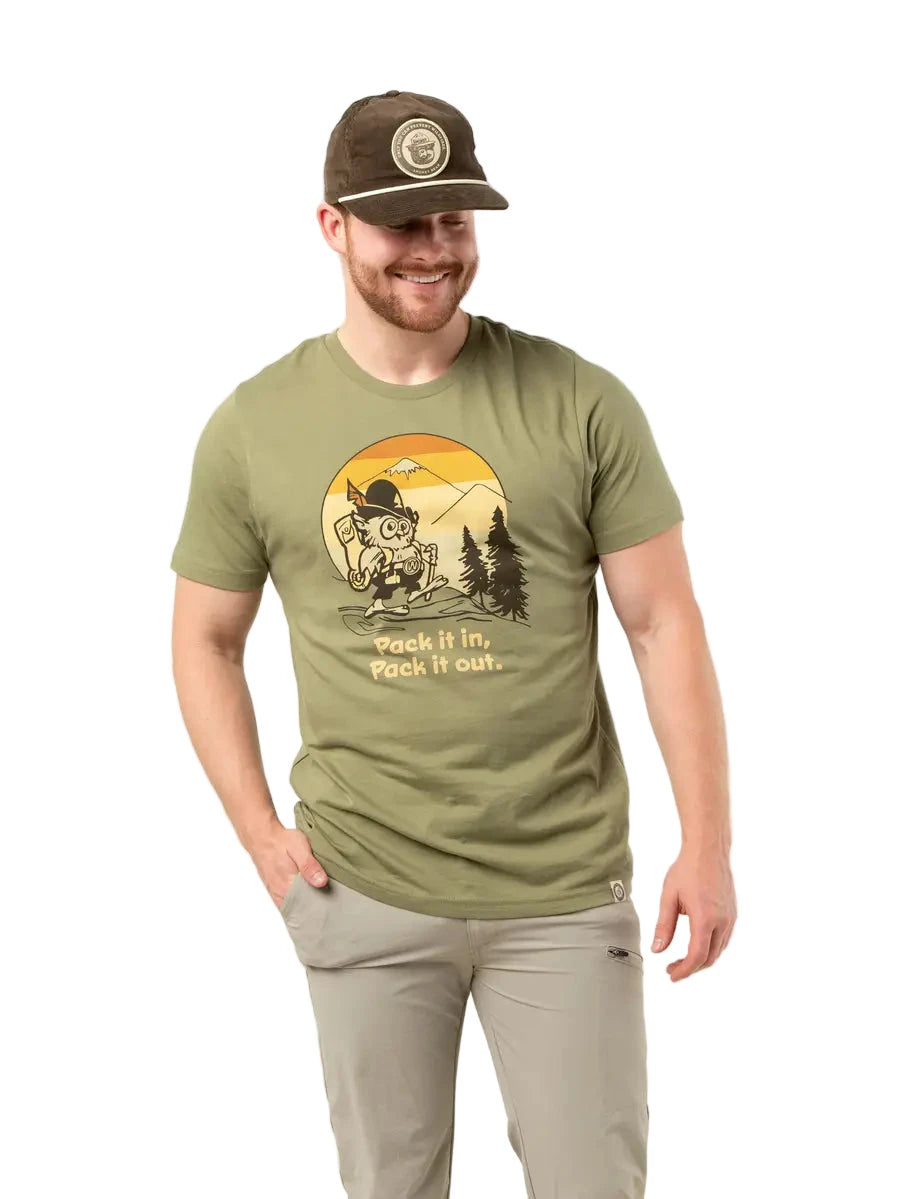 Smiling man wears Landmark Project Unisex Woodsy Owl T-Shirt, Pack It In Pack It Out, with scenic hiking design outdoors.