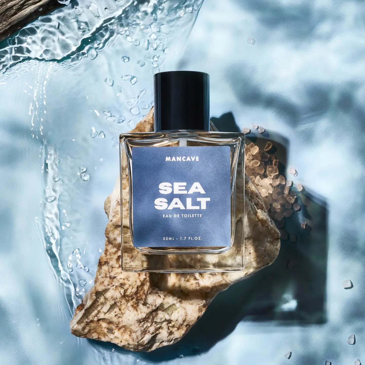 ManCave Sea Salt Eau De Toilette Spray 50ml on a rock with sea salt crystals and ocean water—fresh men's fragrance perfume shot.
