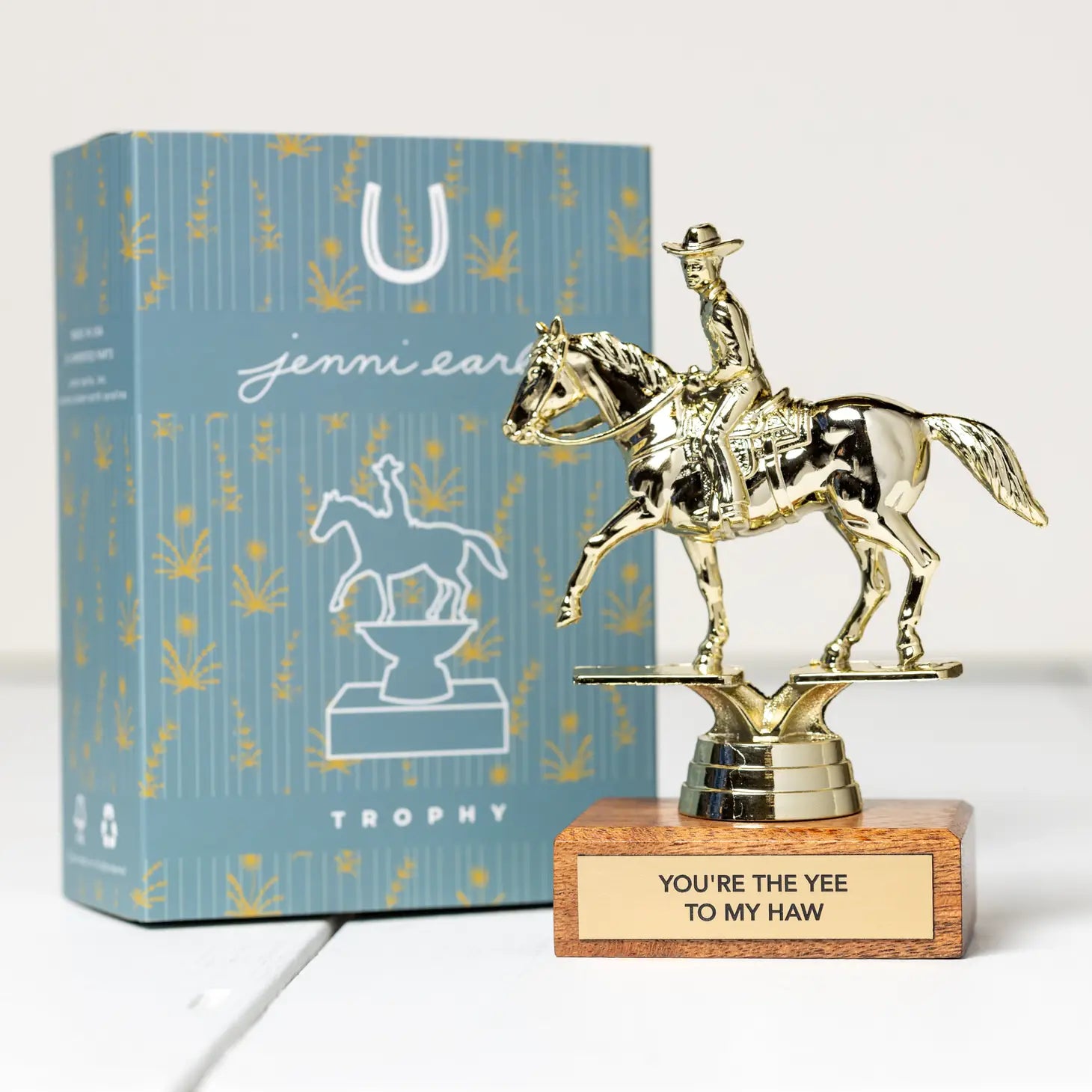 The Jenni Earle Cowboy Trophy - You're The Yee To My Haw features a cowboy on a horse figurine mounted on an FSC certified wooden base, with an inscribed plaque reading "You're the Yee to My Haw," and is presented alongside a blue, cowboy-themed decorative recyclable gift box.