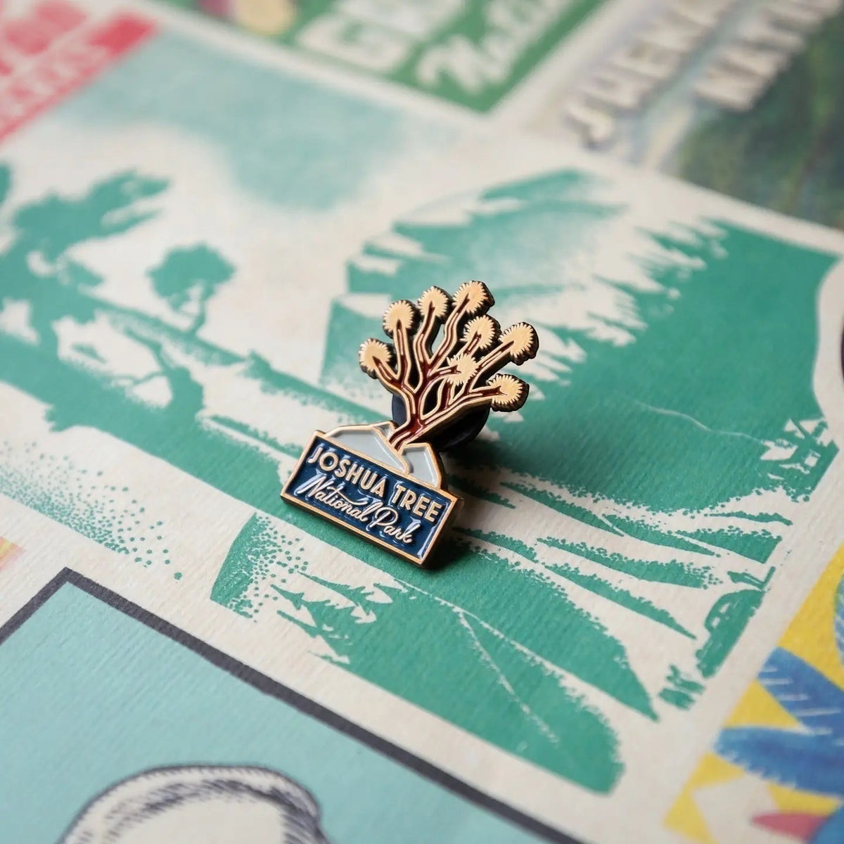 Shop The Landmark Project Joshua Tree Souvenir Enamel Pin displayed on a vibrant, colorful illustrated background surface.