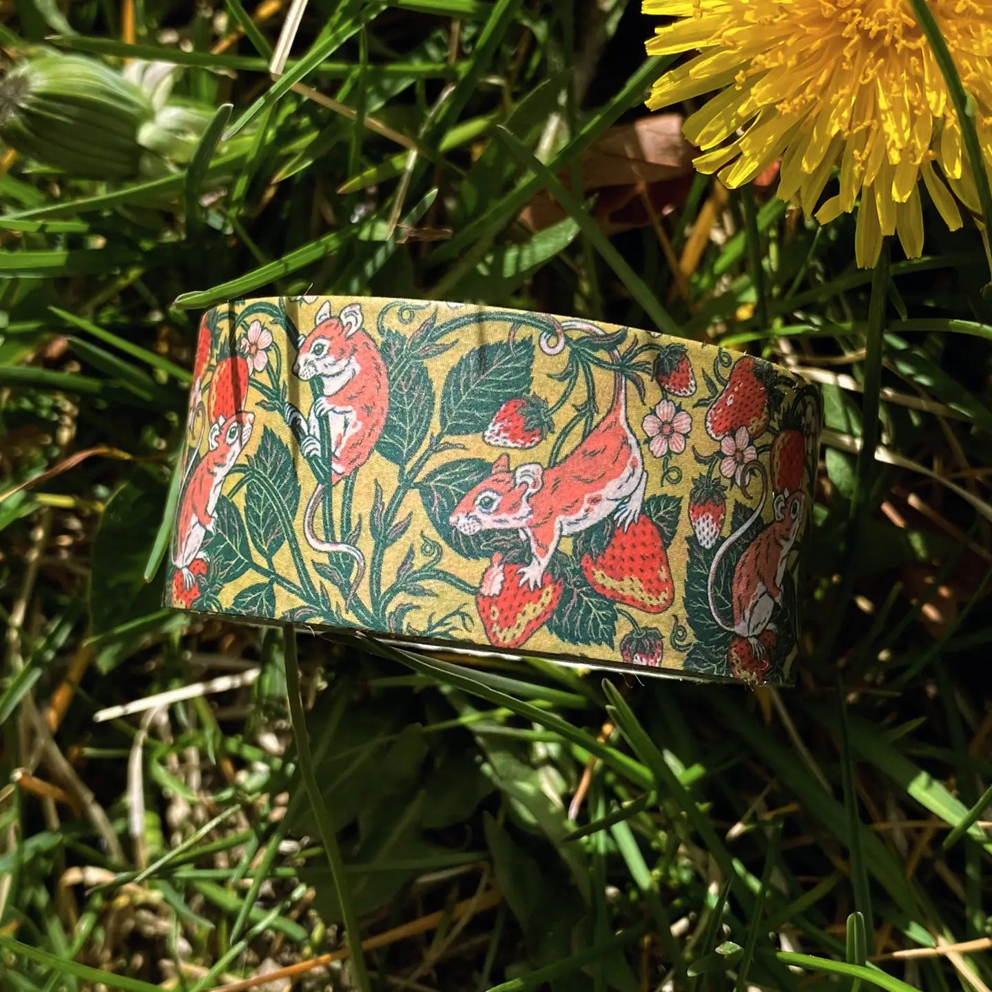 Kate O’Hara Strawberry Mouse Washi Tape with cute mice, strawberries, leaves sits next to a bright yellow dandelion flower.