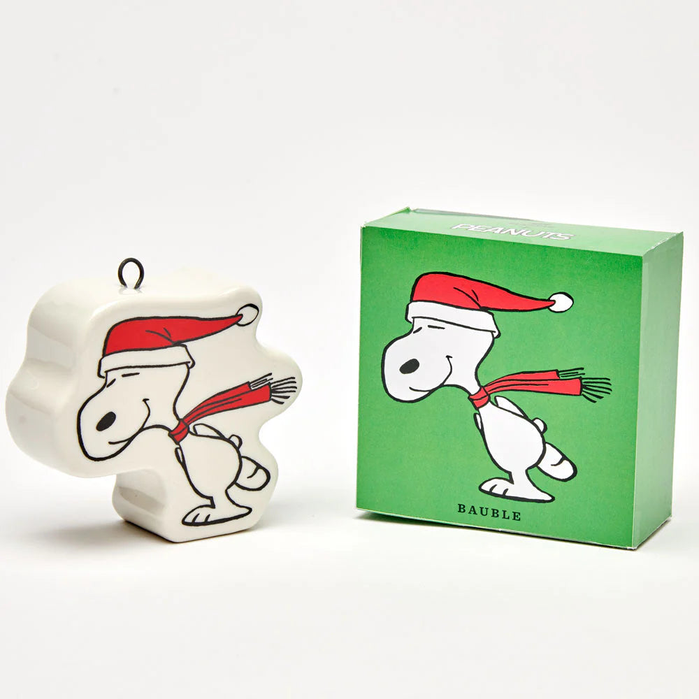 A shaped decoration made from ceramic with a eyelit ring at the top. Design eatures an illustrative Snoopy ice-skating with a red scarf and Santa hat.