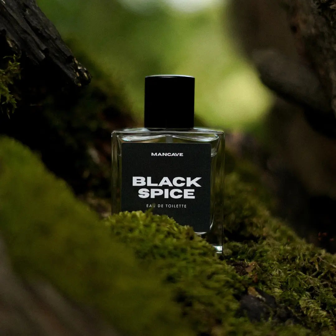 ManCave Black Spice Eau De Toilette Spray 50ml on moss with wood, natural outdoor setting, men's fragrance, premium cologne bottle.