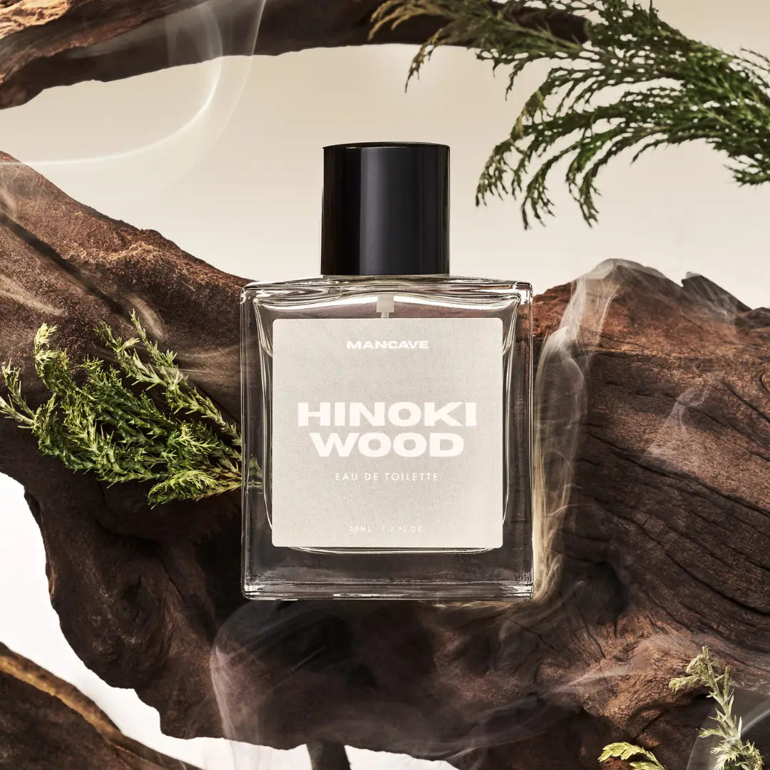 ManCave Hinoki Wood Eau De Toilette Spray 50ml bottle nestled in green leaves, highlighting its fresh woody aroma appeal.