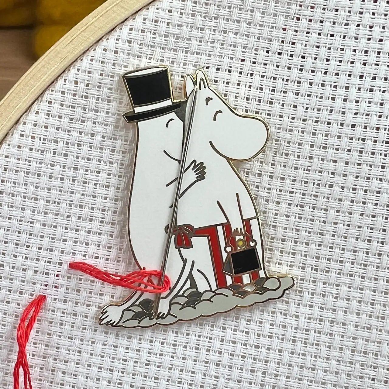 The Crafty Kit Co Moomin Needle Minder features a Little My character with a mischievous expression, dressed in red and holding a needle with pink thread. This charming embroidery accessory comes equipped with a strong magnet to keep your project secure.