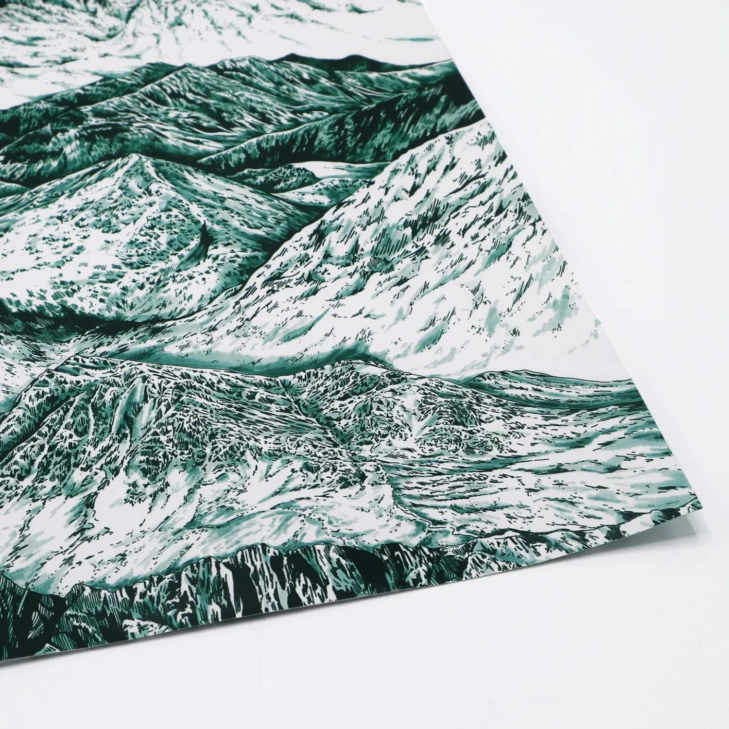 A close-up of a sheet of wrapping paper featuring a detailed, artistic illustration of mountain landscapes in shades of green and white, with the paper slightly curled at the edge."