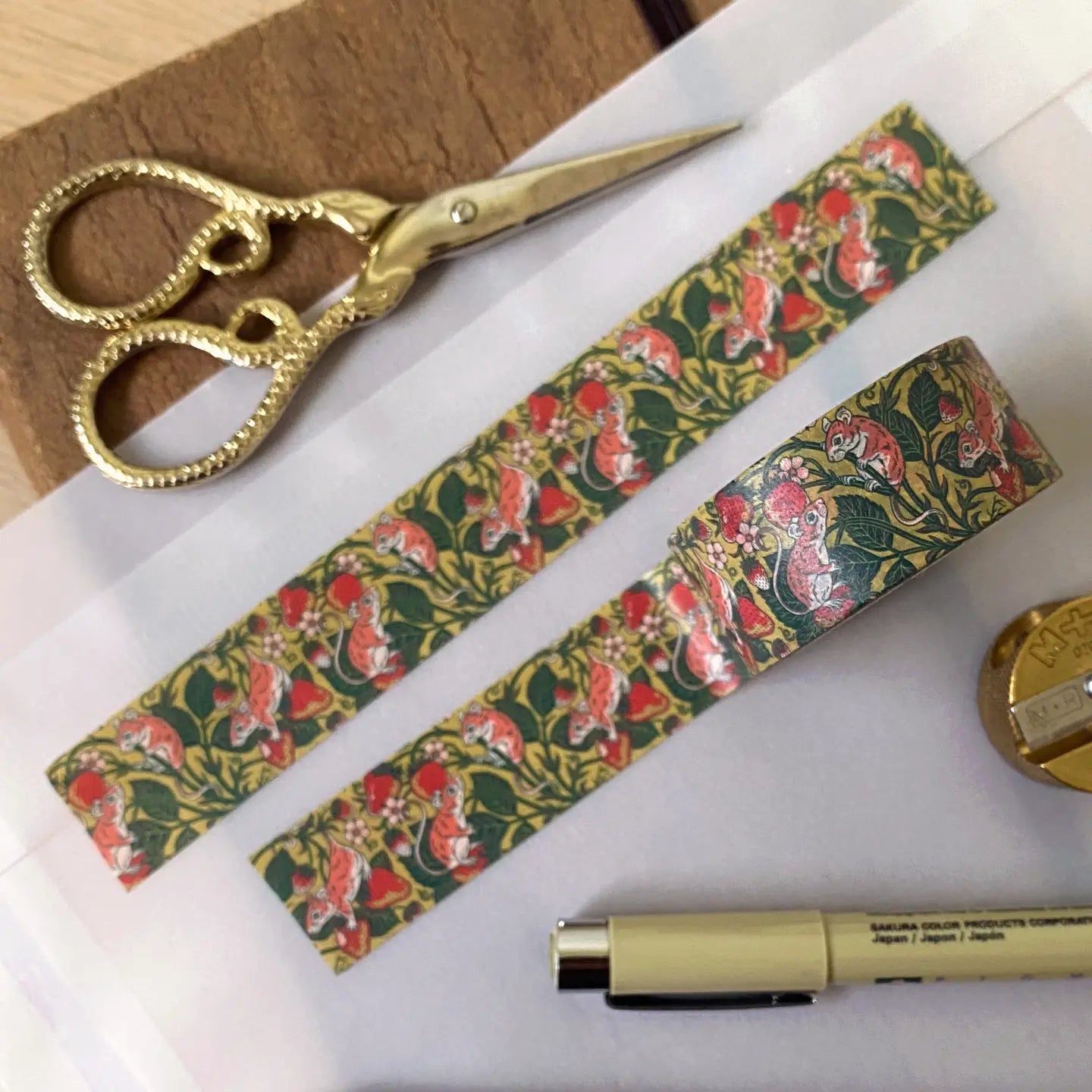 Gold scissors, cottagecore stationery, pen, and Strawberry Mouse washi tape by Kate O’Hara arranged on a desktop workspace.