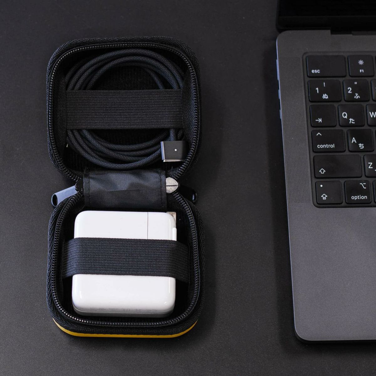 Hightide Nahe Hardshell Case Mini Orange with charger, cable, next to laptop keyboard on dark desk—stylish tech gear organizer.