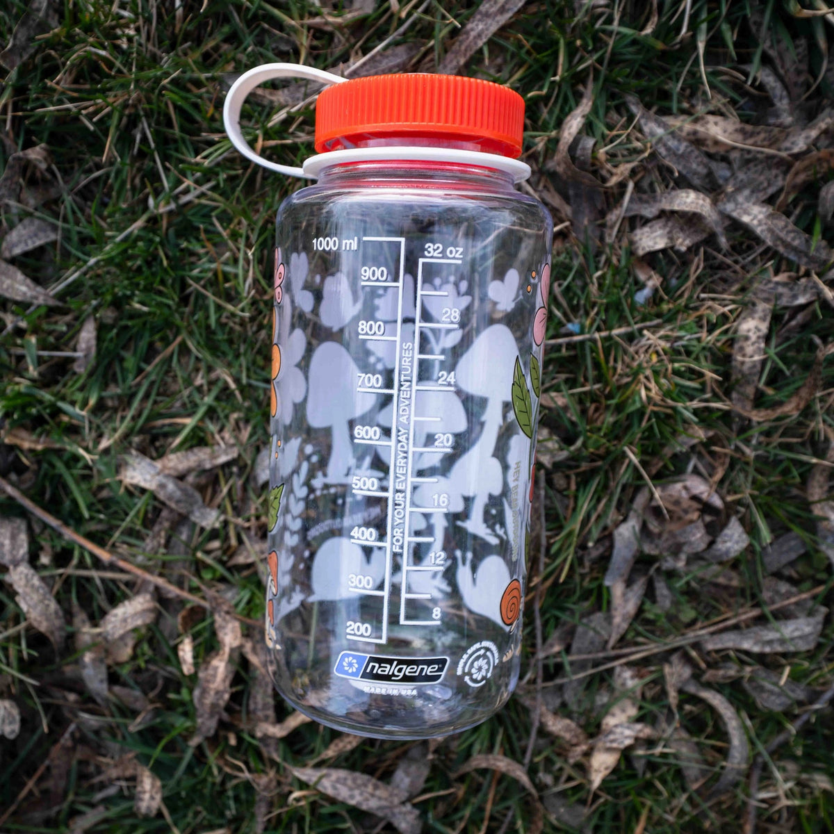 Forager Provisions LTD 32oz Nalgene water bottle with mushroom graphics, resting on a bed of dry grass and leaves.