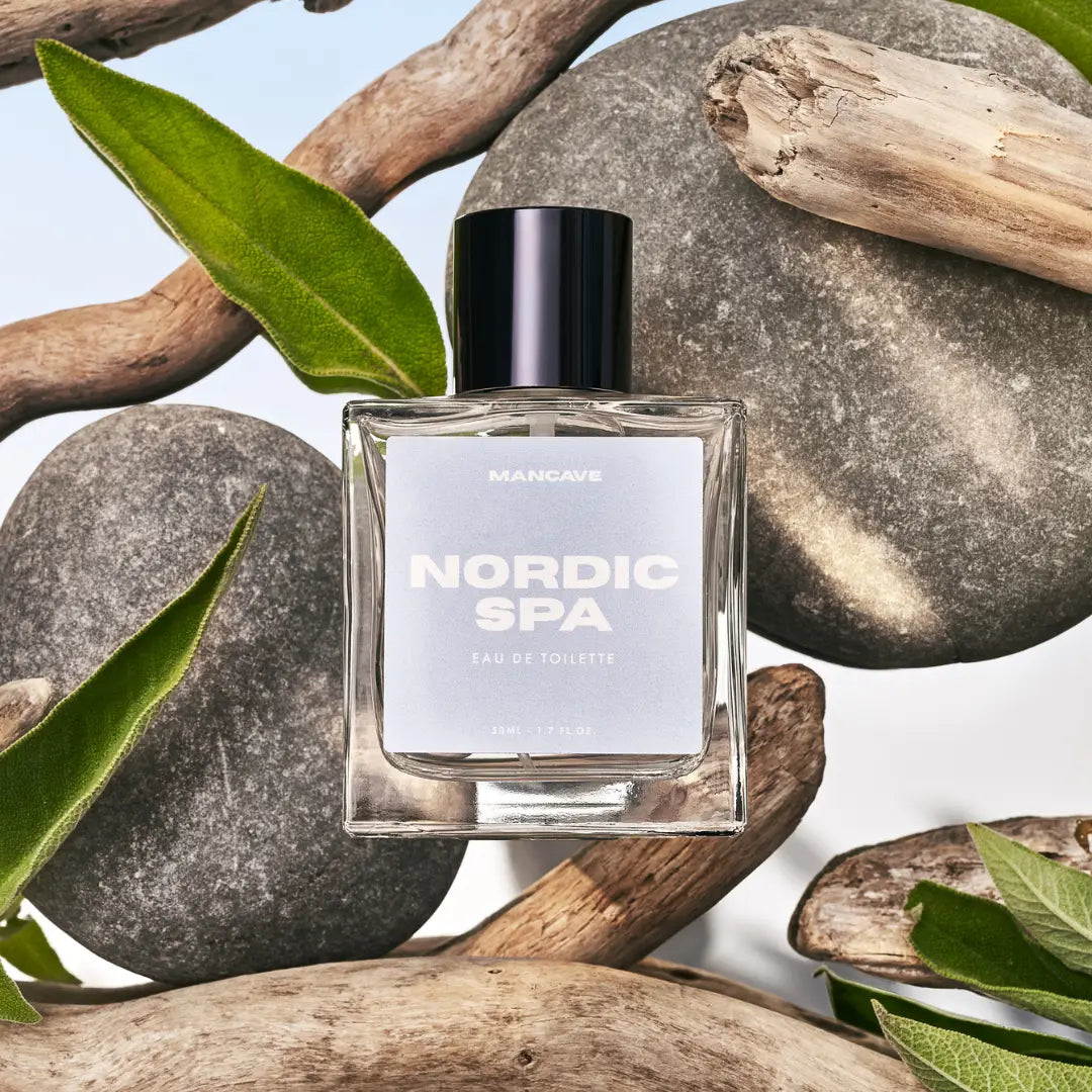 ManCave Nordic Spa Eau De Toilette Spray 50ml bottle displayed with natural stones, green leaves, and driftwood for men’s scent.